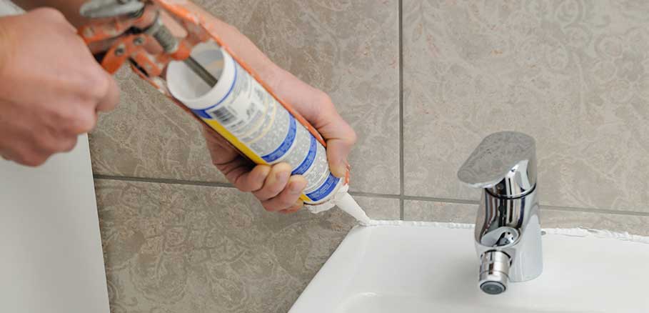 Άντρας κλείνει ρωγμές σε νιπτήρα μπάνιου με εργαλείο σιλικόνης